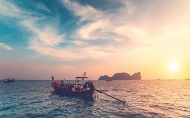 The traditional fishing boats with the tourists in the ocean next to the exotic Phi Phi Islands, the Kingdom of Thailand. Breathtaking colorful sunset background. Beauty of wild nature.