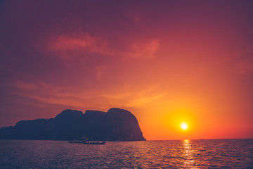 Fototapeta na wymiar Breathtaking sunset over the ocean and limestone cliffs next to the exotic Phi Phi Islands, the Kingdom of Thailand. Amazing sky in the golden, orange and scarlet tints.