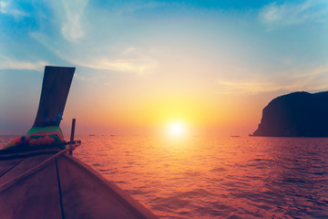 Close up image of the bow of the traditional fishing wooden boat. Breathtaking colorful sunset over the ocean and limestone cliff next to the exotic Phi Phi Islands, the Kingdom of Thailand.