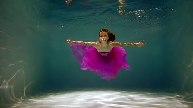 brave young girl floating in a dress of fuchsia under water