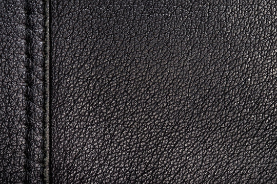 Texture of a surface from a natural skin of black color with single seam with double stitch in left side. Close-up view.
