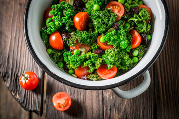 Kale salad with tomatoes, peas and cranberry on wooden table