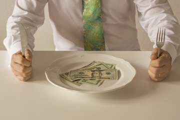 Money on a plate being cut like food with a knife and fork