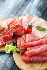 Food tray with delicious salami, pieces of sliced ham, sausage, tomatoes, salad and vegetable - Meat platter with selection