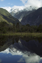 Paisaje de picos de montañas nevados y verdes con cielo nublado reflejado en un lago  en Nueva Zelanda