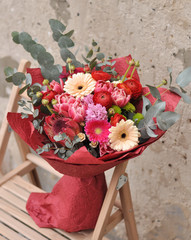 Flower arrangement of pions, gerberas, exotic flowers and eucalyptus. A magnificent bouquet on a chair near the wall. Florist's work © Tamara