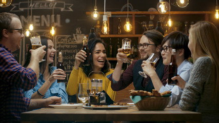 Diverse Group of Friends Celebrate with a Toast and Clink Raised Glasses with Various Drinks in Celebration. Beautiful Young People Have Fun in the Stylish Bar/ Restaurant.