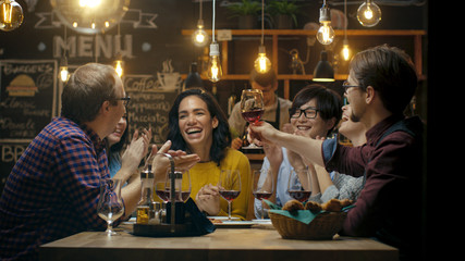 Diverse Group of Friends Celebrate with a Toast and Raise Wine Glasses in Celebration. Beautiful Young People Have Fun in the Stylish Bar/ Restaurant.
