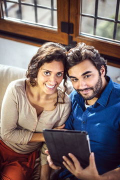 Young Couple Sitting On Sofa Using Digital Tablet