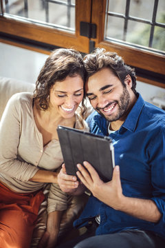 Young Couple Sitting On Sofa Using Digital Tablet