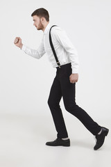 Freeze action full length sideways shot of fashionable young European businessman with stubble walking fast against blank studio wall background with copy space for your advertising content