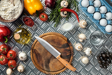 Cutting wooden board with traditional pizza preparation ingredients: mushrooms, tomatoes sauce, basil, olive oil, cheese, spices. Iron texture table background
