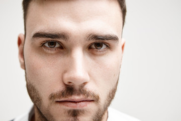 Close up highly detailed studio portrait of handsome young brown eyed European man with well trimmed mustache and beard posing isolated at blank wall with copy space for your promotional information