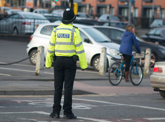 policeman shrugs his shoulders in wrong size hi vis vest middle of road with cyclist in background