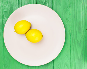 Two yellow lemons on a pink plate on a green wooden background.