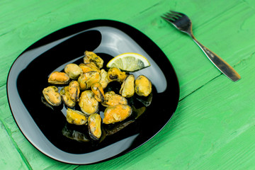 Mussels on a black plate on a wooden green background.