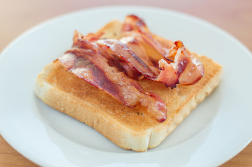 Fried bacon on toast on white plate.