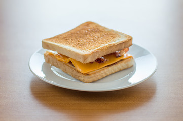 Toast with cheese and bacon on white plate.