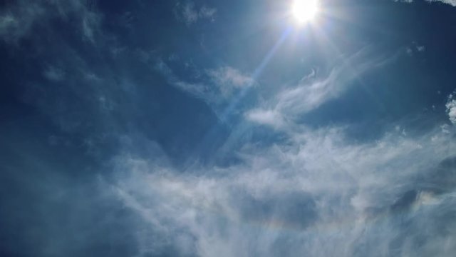 White clouds moving high over blue sky background, sun shining. 4K UHD Timelapse