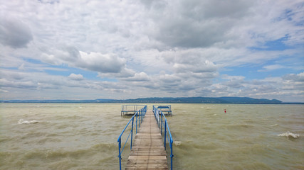 First-person shot of a jetty on a lake, puffy clouds against a clear blue sky