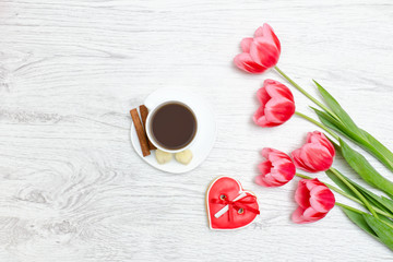 Fototapeta na wymiar Pink tulips, mug of coffee and red gingerbread. Light wooden background.