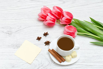Fototapeta na wymiar Pink tulips, mug of coffee and cinamon. Empty postcard. Llight wooden background.