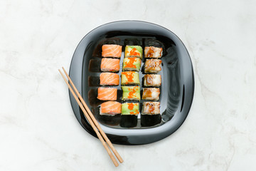 Black plate with various rolls and chopsticks. Top view