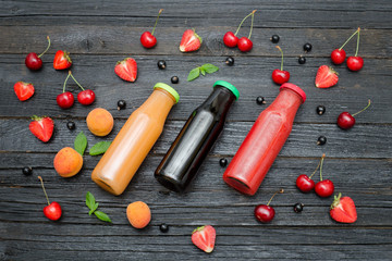 Fototapeta na wymiar Three bottles of juice and fruits on black wooden background. Food concept