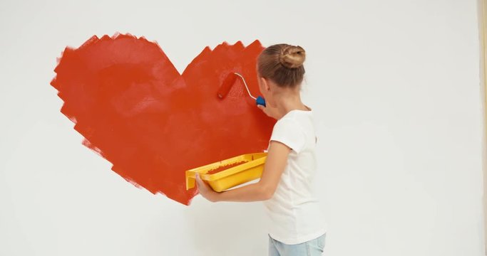 Child painting on the wall a big red heart