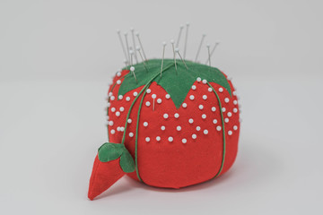 Studio shot of an isolated red pin cushion in the shape of a strawberry, stuck with white glass pins