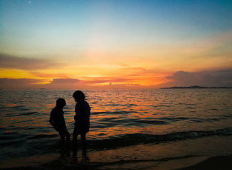 Beautiful of  The silhouette of a boy and a girl playing sea water at the beach at sunset.