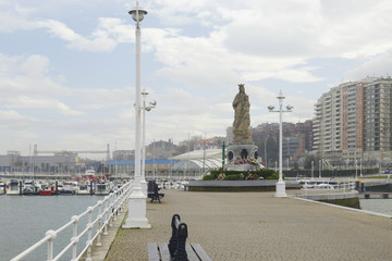 Fototapeta na wymiar Blessed Virgin Mary statue in the fishing port of Santurtzi, Basque Country, Spain. Outdoors on a cloudy day. No people.