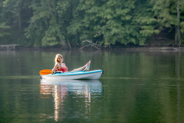 Stunning young blonde Caucasian woman rests in her kayak on a lake that is still