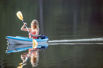Stunning young blonde Caucasian woman paddles in a canoe on a still lake