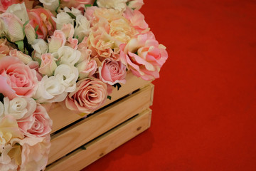 Artificial white and pink rose flowers in wooden crate on red carpet