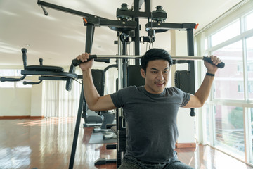Fototapeta na wymiar Handsome man playing with fitness machine in gym. Bodybuilder man doing heavy weight exercise with machine with cable in fitness club.