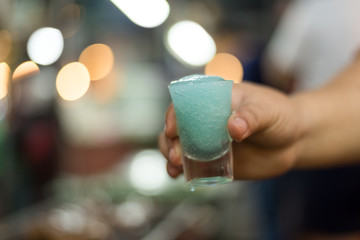 Obraz na płótnie Canvas Hand hold cold Blue Maitai cocktail with bokeh blur light background