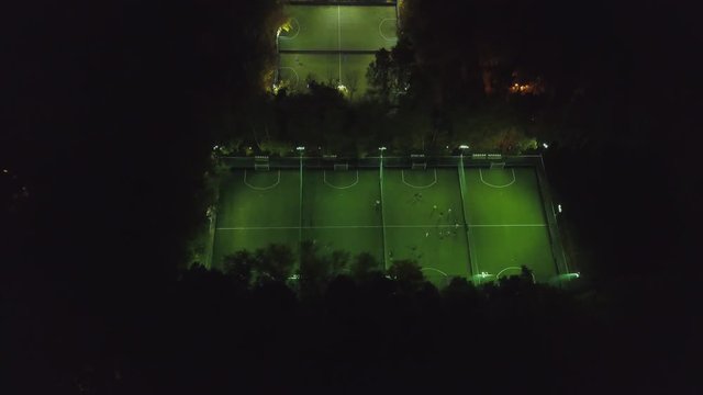 Aerial view of football pitch at night with amateur football players playing the game in the city. Clip. Football soccer field night aerial