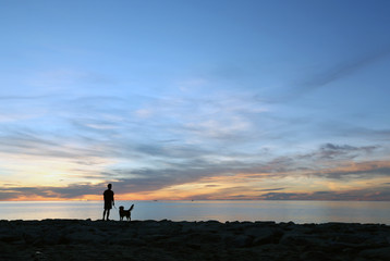 Silhouette a man with a dog on the beach at sunrise in the south of Thailand.Golden retriever silhouette on the beach.Travel with dog.