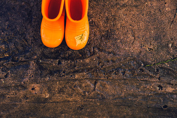 Orange rubber wellington boots on a grungy concrete wet surface. Top view, horizontal.