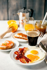 The English breakfast - eggs,  bacon,  toasts with ricotta and jam, juice in a glass, coffee on a grey background. Selective focus.