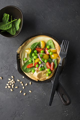 Dutch baby pancake for breakfast with vegetables, herbs and nuts: spinach, pine nuts, cherry tomatoes, sweet onions, in white ceramic form. Top view.