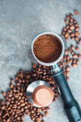 Equipment for brewing coffee flat lay. Portafilter with ground coffee, tamper, and beans on a concrete background with copy space.