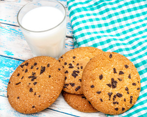 Chocolate chip cookies, glass of milk and kitchen towel on the old blue wooden table.
