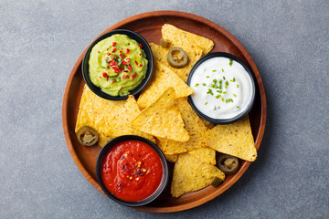 Nachos chips with dip variety on a wooden plate.