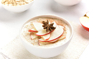 Bowl of oats porridge with red apple slices and cinnamon