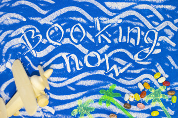Booking now inscription on a blue colored sand with waves, candies, toy airplane, top view, flat lay