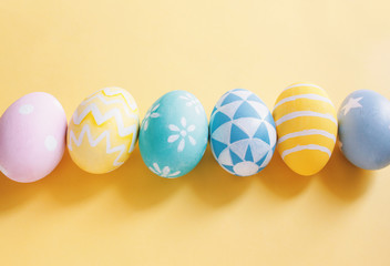 Row of pastel and colorful easter eggs with copy space on yellow background.