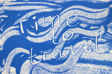 Time to travel inscription on a blue colored sand with waves, top view, flat lay