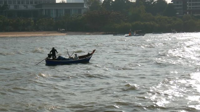 Two Thai fishermen sail on small wooden boat on strong waves to fish